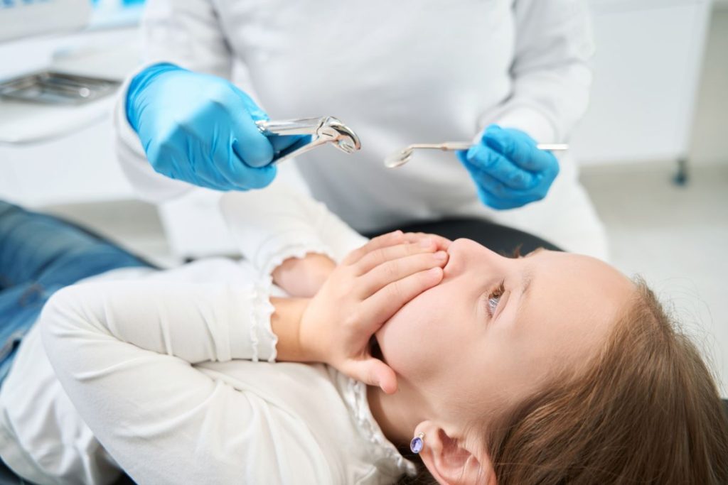 Pediatric dentist applying fluoride treatment to child's teeth in dental office.