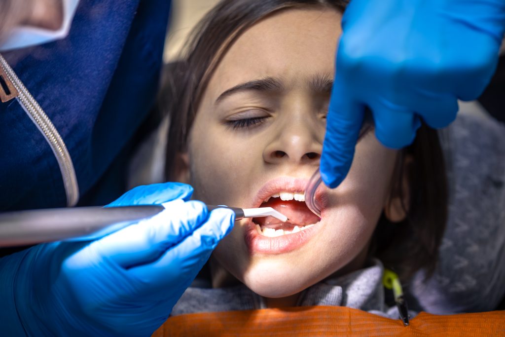 Dental professional in blue gloves examining young patient's teeth during dental checkup.