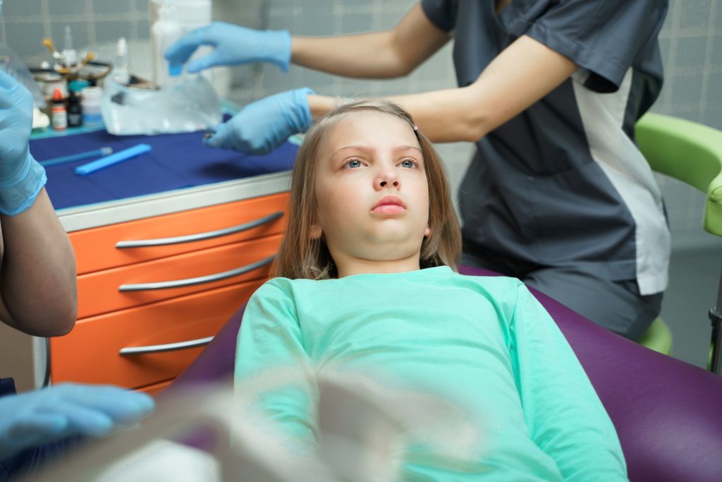 Young girl in dental chair receiving examination from dentist wearing blue gloves in modern clinic.