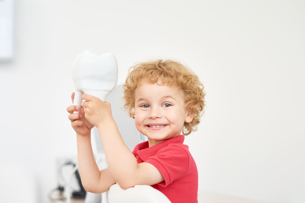 Happy toddler with curly hair holding light bulb in bright room.